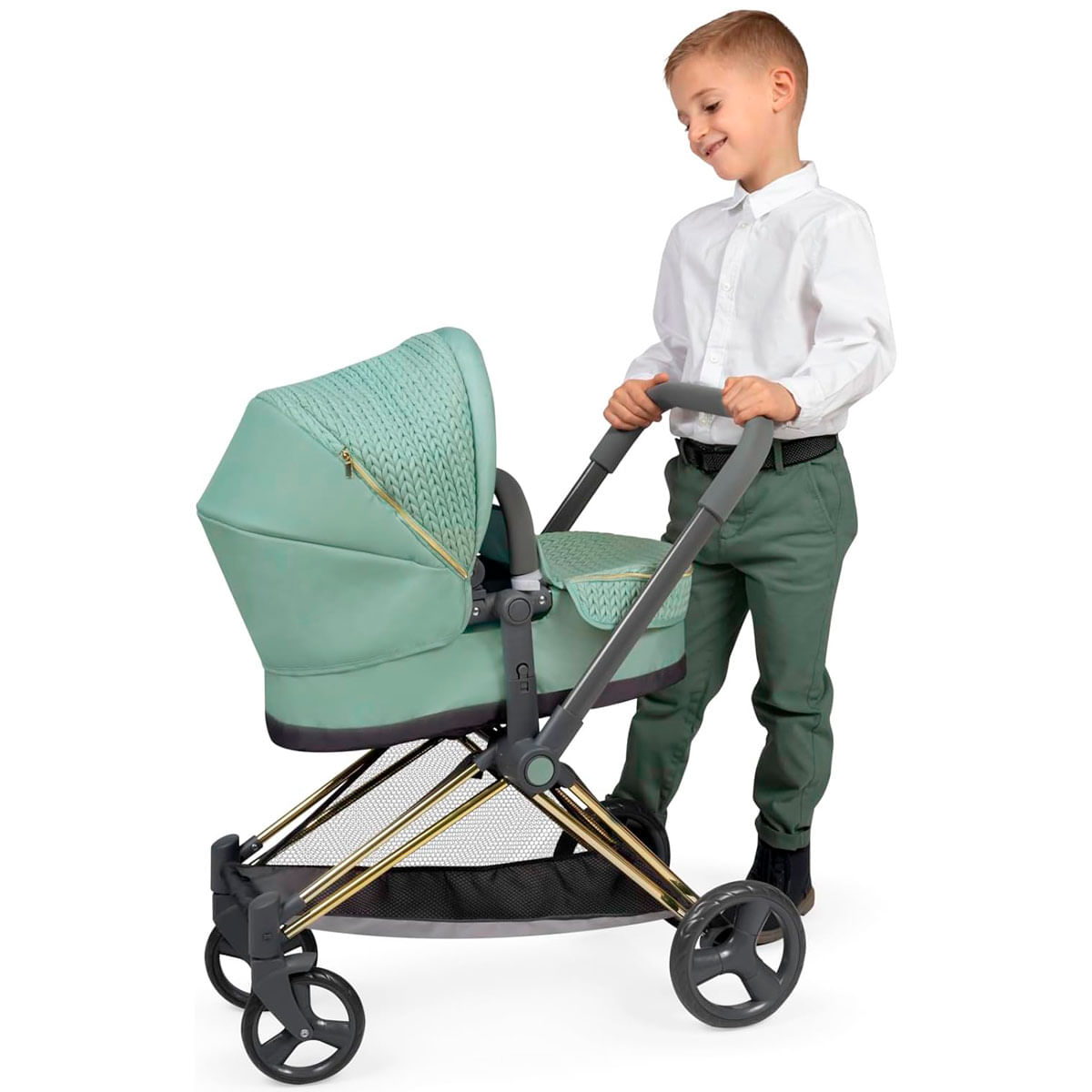 Un niño con camisa blanca y pantalones verdes empuja un cochecito verde menta. El cochecito tiene detalles dorados y ruedas negras.