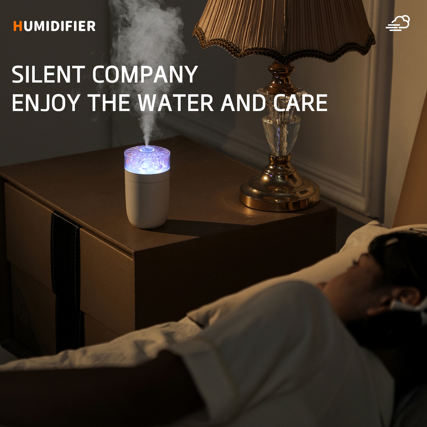 Ein Luftbefeuchter auf einem Nachttisch mit einer Lampe. Eine Person schläft im Bett. Der Text lautet 'Silent Company Enjoy the Water and Care'.
