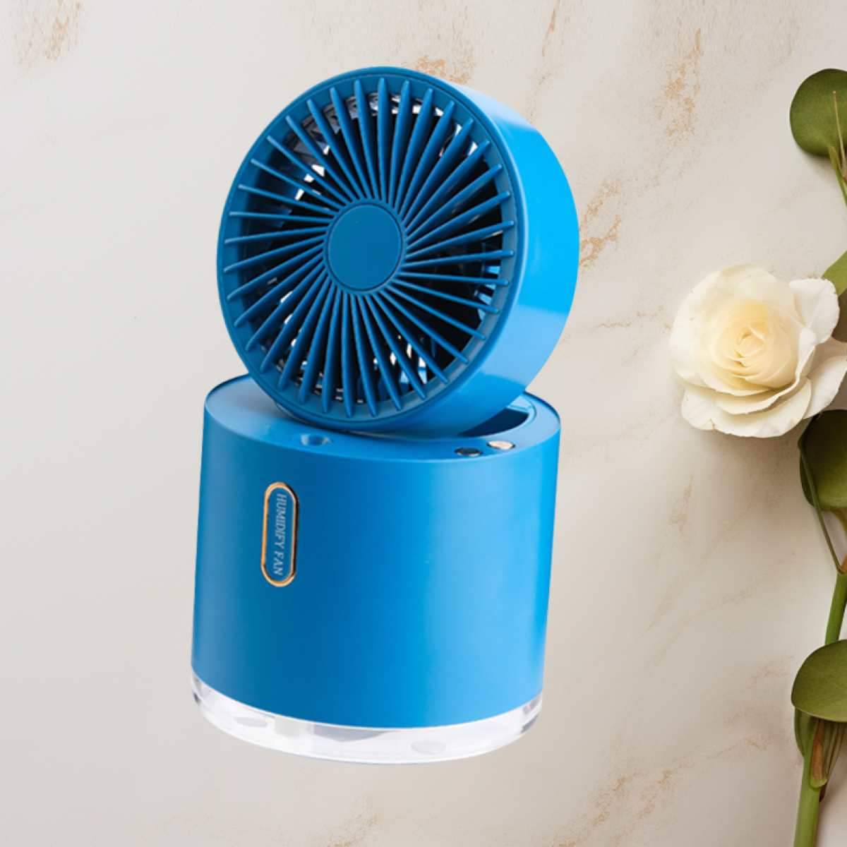 Un ventilador humidificador azul está sobre una superficie con una rosa blanca y hojas verdes. El ventilador tiene una base cilíndrica y una cabeza de ventilador.