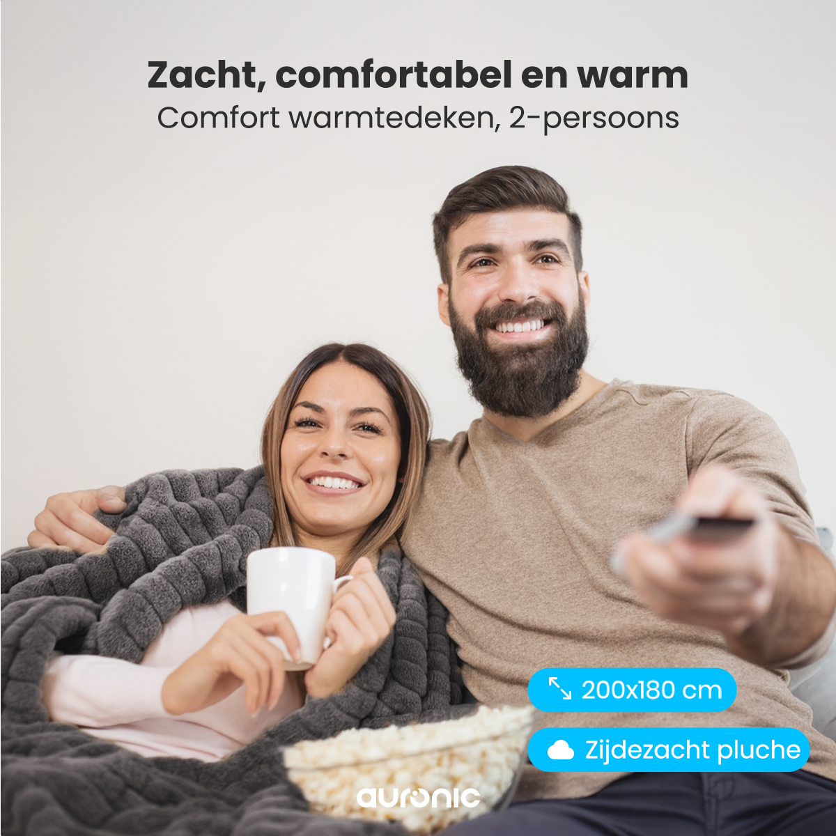 Een lachend stel, gehuld in een grijze deken. De vrouw houdt een mok vast, popcorn staat vooraan. Man houdt een afstandsbediening vast.