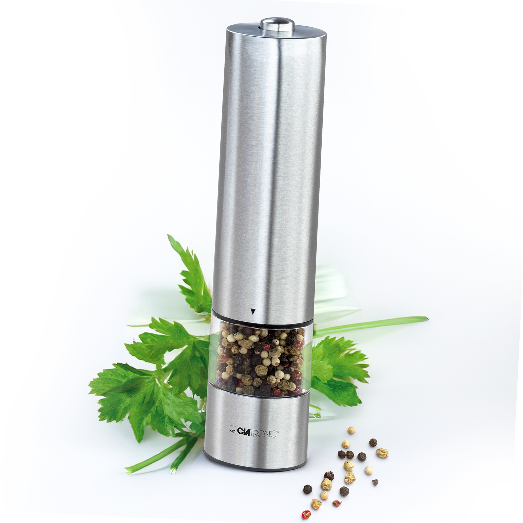 Stalowy młynek do pieprzu z ziarnami pieprzu i zieloną pietruszką na białym tle. Młynek jest ustawiony pod kątem.