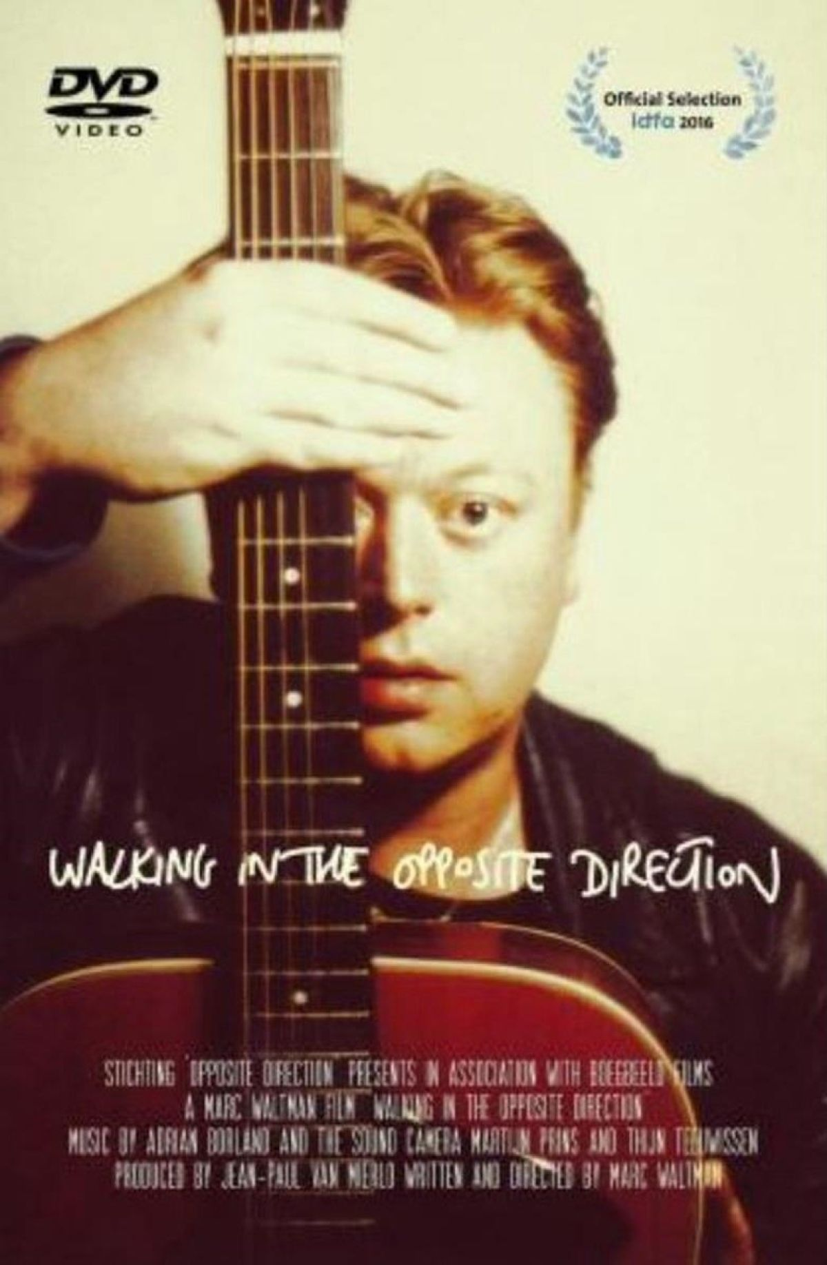 Een man houdt een gitaar vast en bedekt een deel van zijn gezicht. De titel 'Walking in the Opposite Direction' is geschreven.
