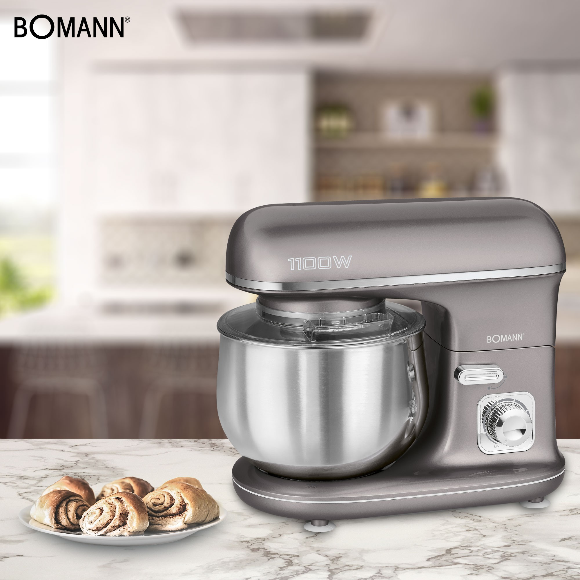 Grauer Bomann-Küchenmixer mit silberner Schüssel und einem Teller mit Zimtschnecken auf Marmortisch.