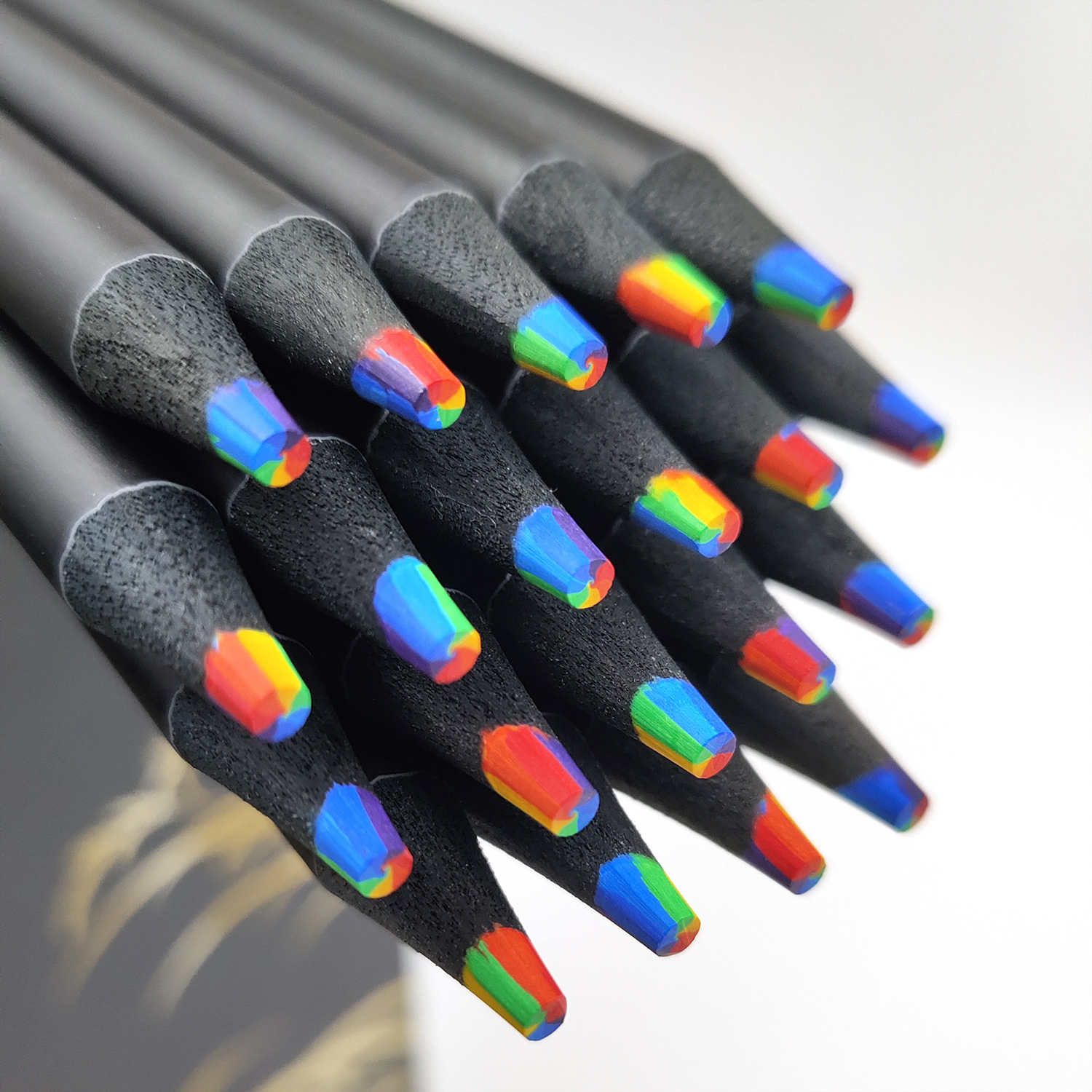 Primer plano de lápices negros con puntas de colores arcoíris. Los lápices están agrupados, mostrando colores vibrantes sobre un fondo blanco.