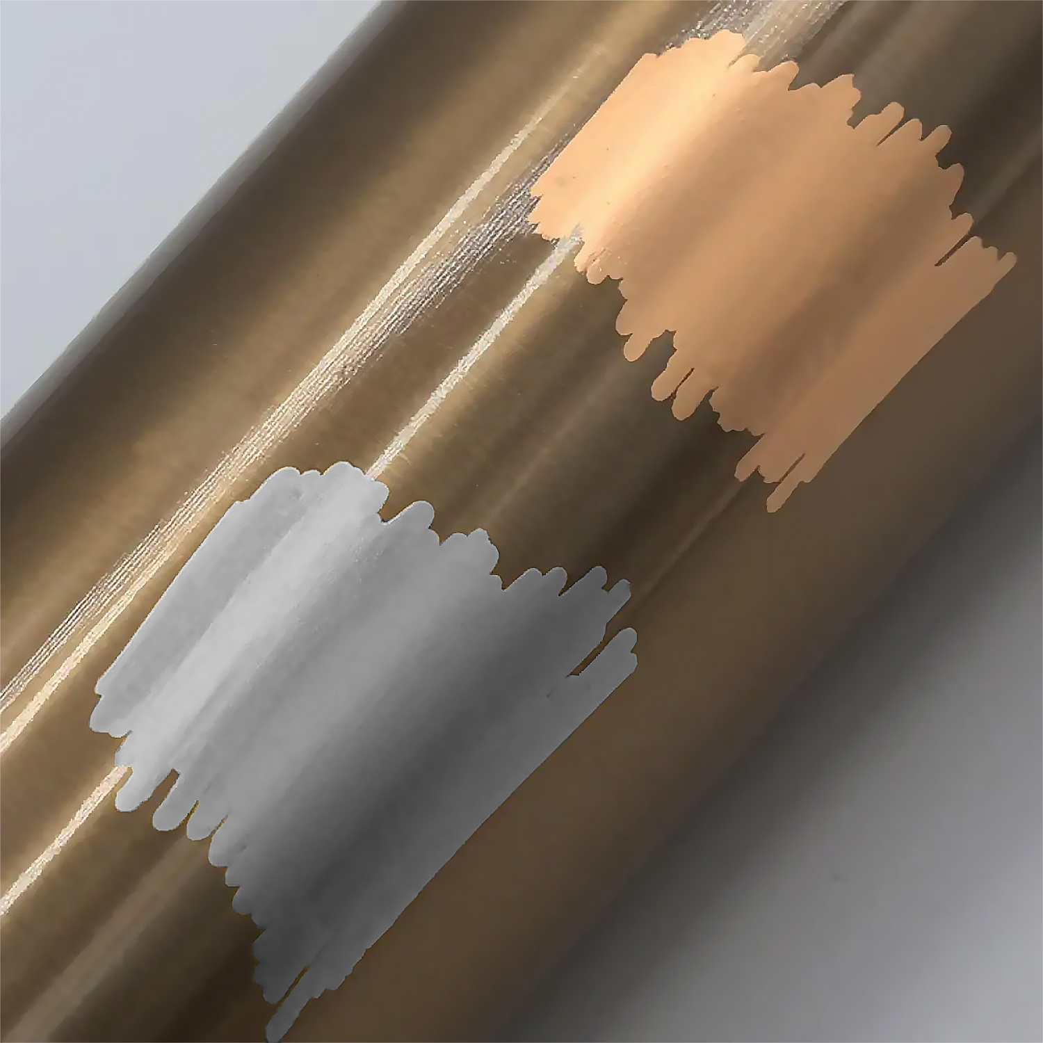 Primer plano de un rollo color bronce con dos pinceladas: melocotón arriba y gris abajo, sobre fondo blanco.