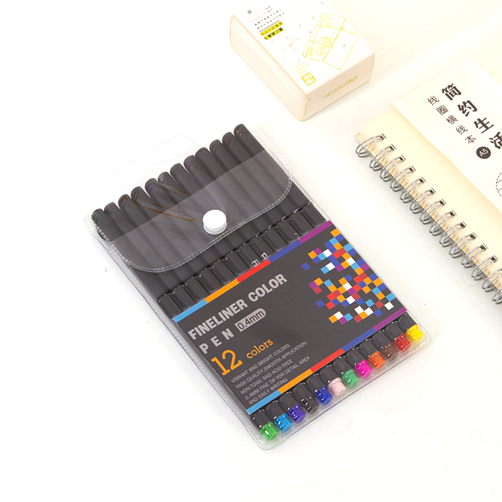Un paquete de 12 rotuladores de color con una funda transparente. Un cuaderno y una caja pequeña en el fondo.