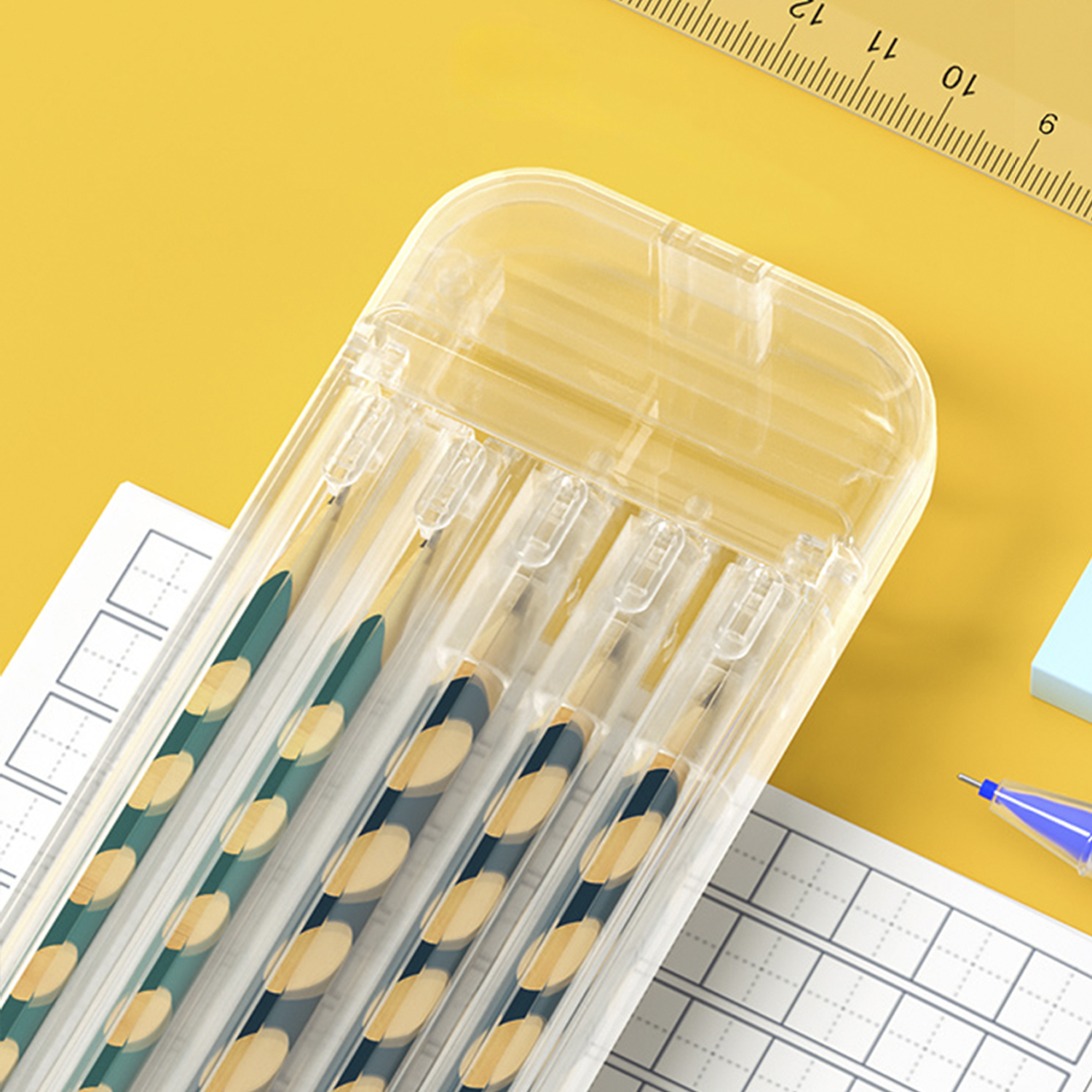 Estuche transparente con bolígrafos. Los bolígrafos tienen patrones verdes y amarillos. También se ven una regla y papel cuadriculado.
