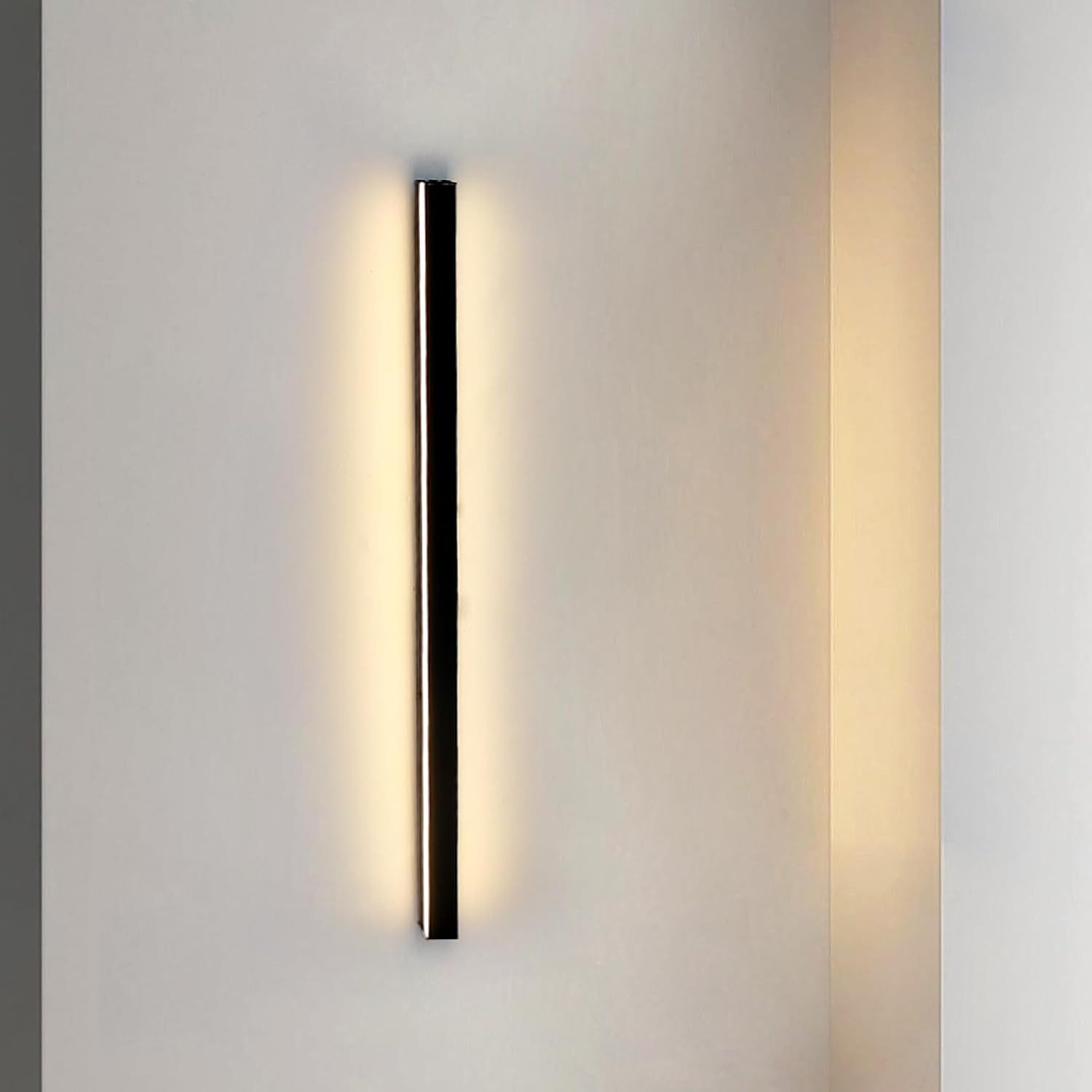 Una lampada da parete moderna con cornice nera e luce brillante. È montata verticalmente su una parete bianca. Lo sfondo ha un angolo.