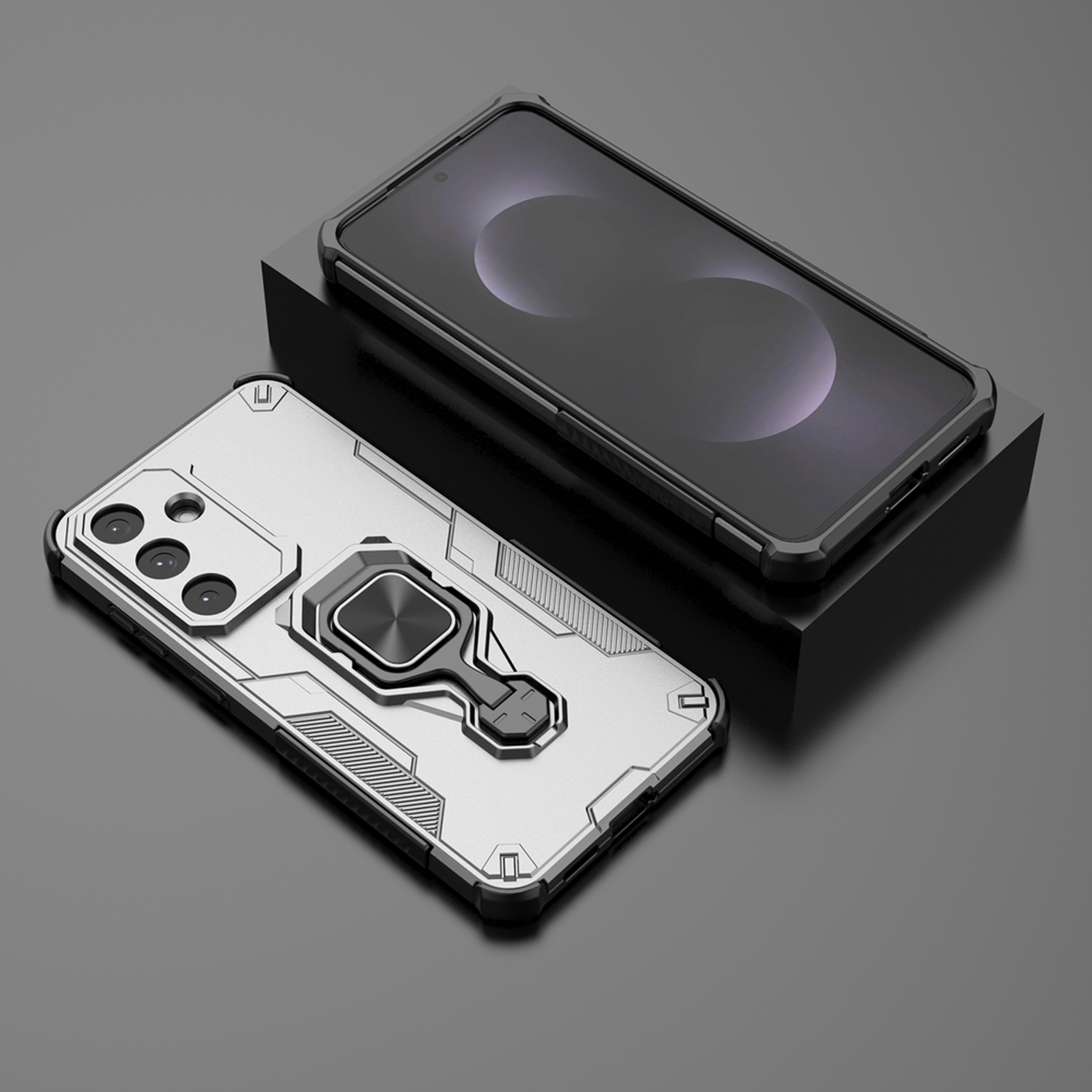 Deux coques de téléphone. Une argentée avec un support à anneau, l'autre noire sur un bloc noir. Fond gris.