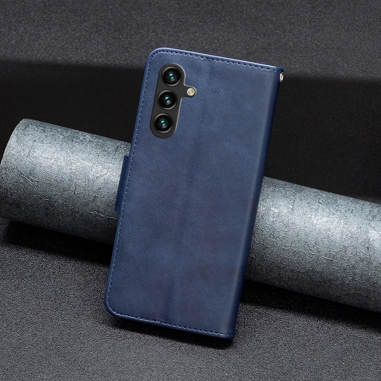 Een blauwe leren telefoonhoes met drie cameralenzen ligt op een donker oppervlak naast een grijs cilindrisch object.