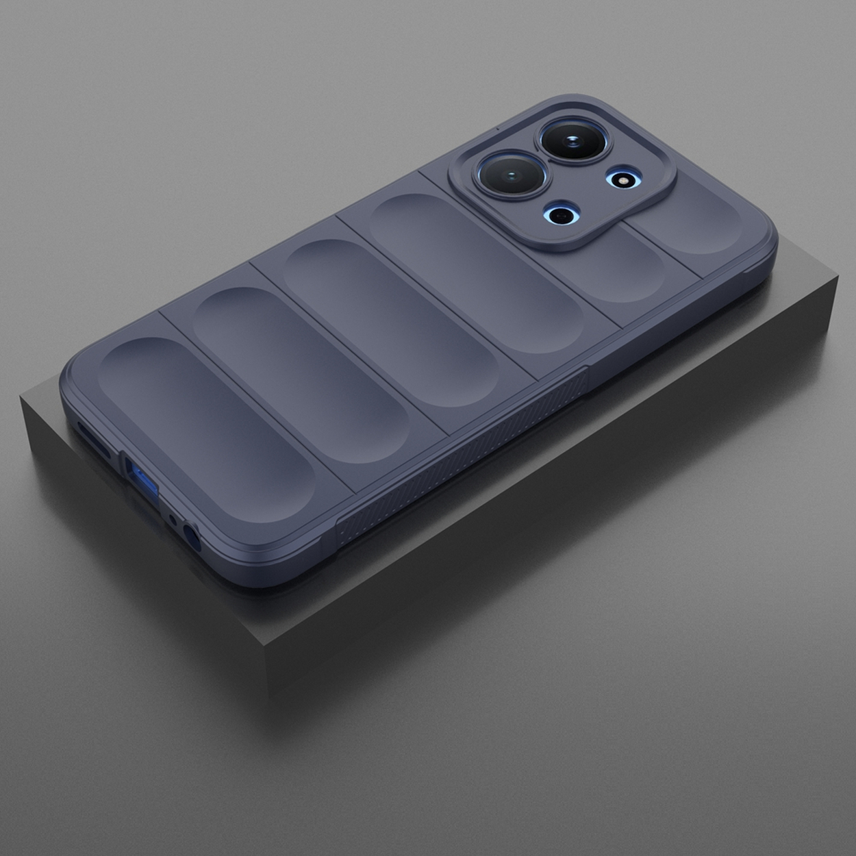 Une coque de téléphone bleu foncé sur une plateforme gris foncé. La coque a des sections rectangulaires en relief et des ouvertures pour les lentilles de la caméra.