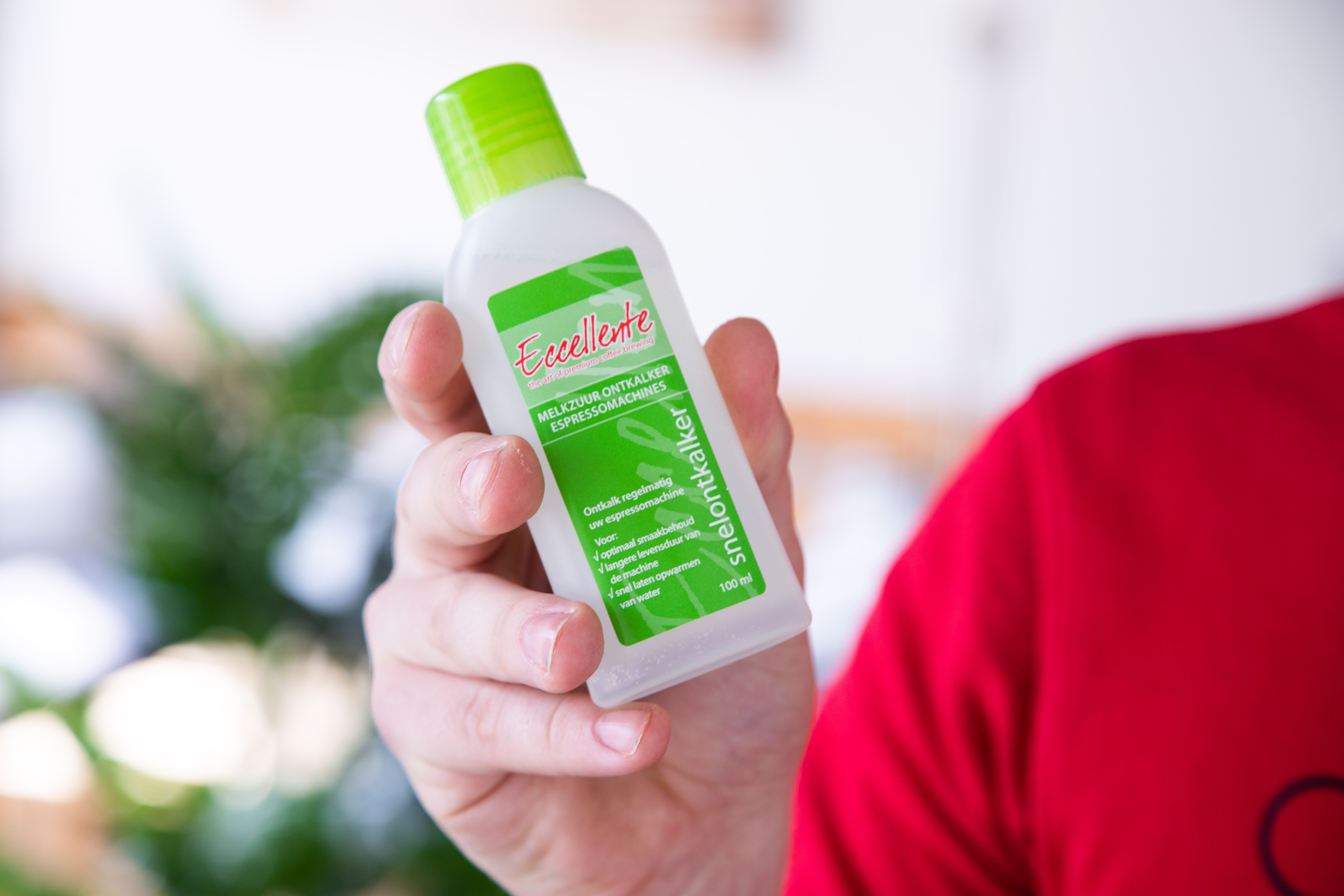 A hand holds a white bottle with green cap. Label says 'Eccellente' and 'snelontkalker'.