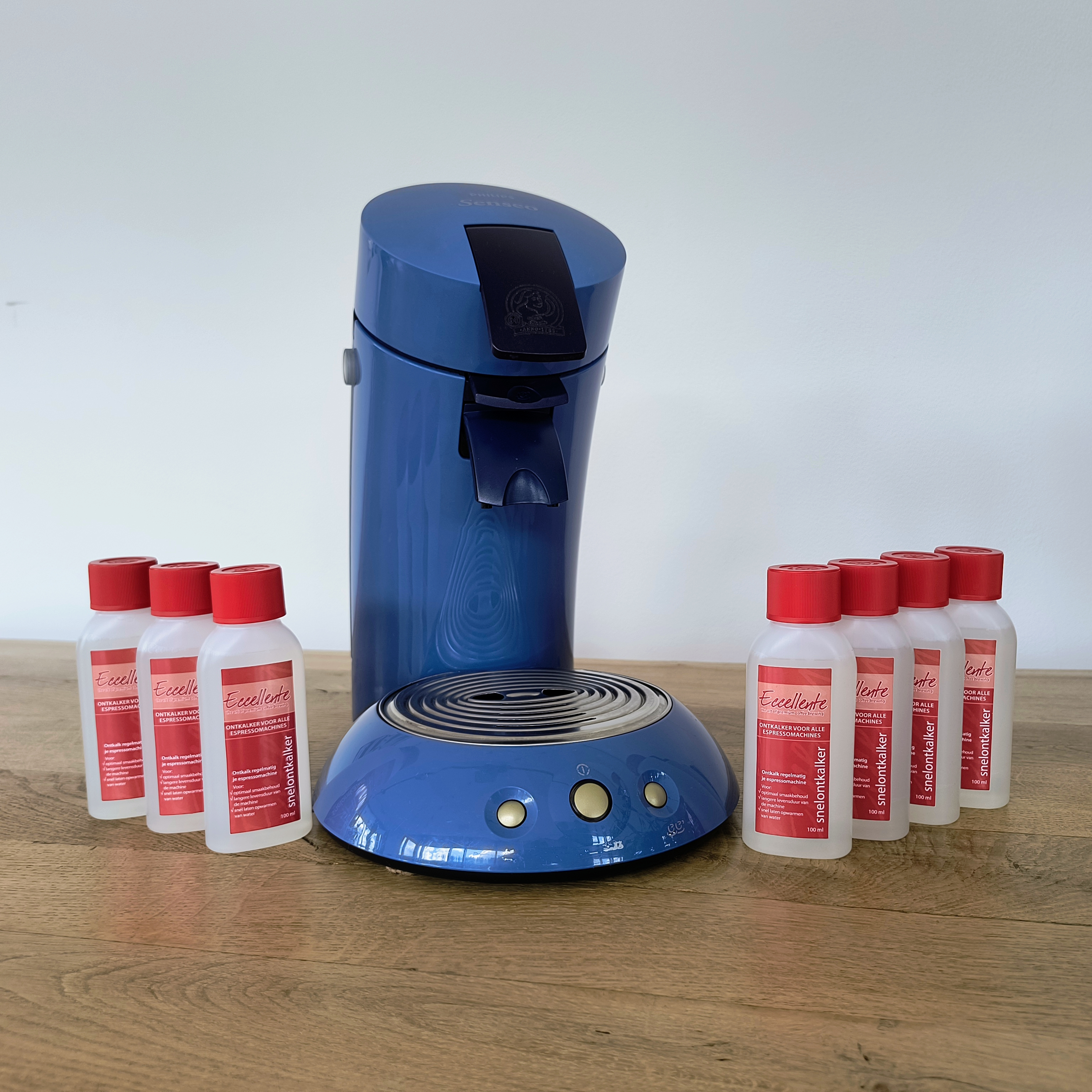 Blauwe koffiemachine met ontkalkerflessen op houten oppervlak, witte achtergrond.