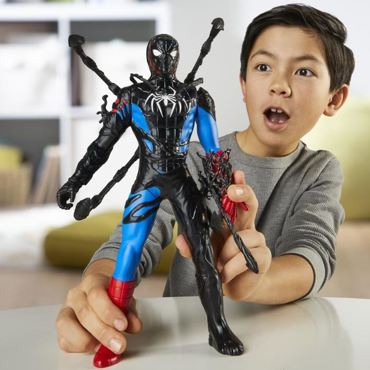 Un niño sostiene una figura de acción de Spider-Man. La figura es negra y azul. El niño tiene la boca abierta y parece sorprendido.