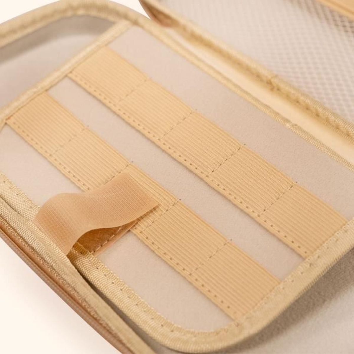 Interior de estuche abierto. Tejido beige con correas elásticas y una correa de velcro. Color marrón claro.