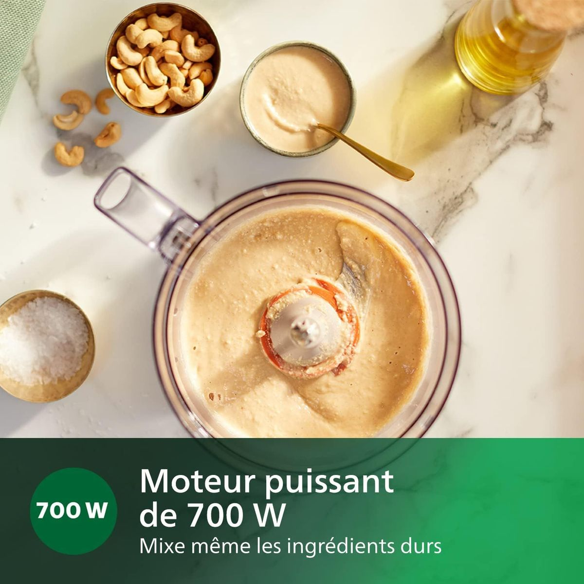 Ein Foodprocessor mit Zutaten: Cashewnüsse, Sauce, Salz und Öl. Der Prozessor mischt Zutaten. Text: 700W Motor.