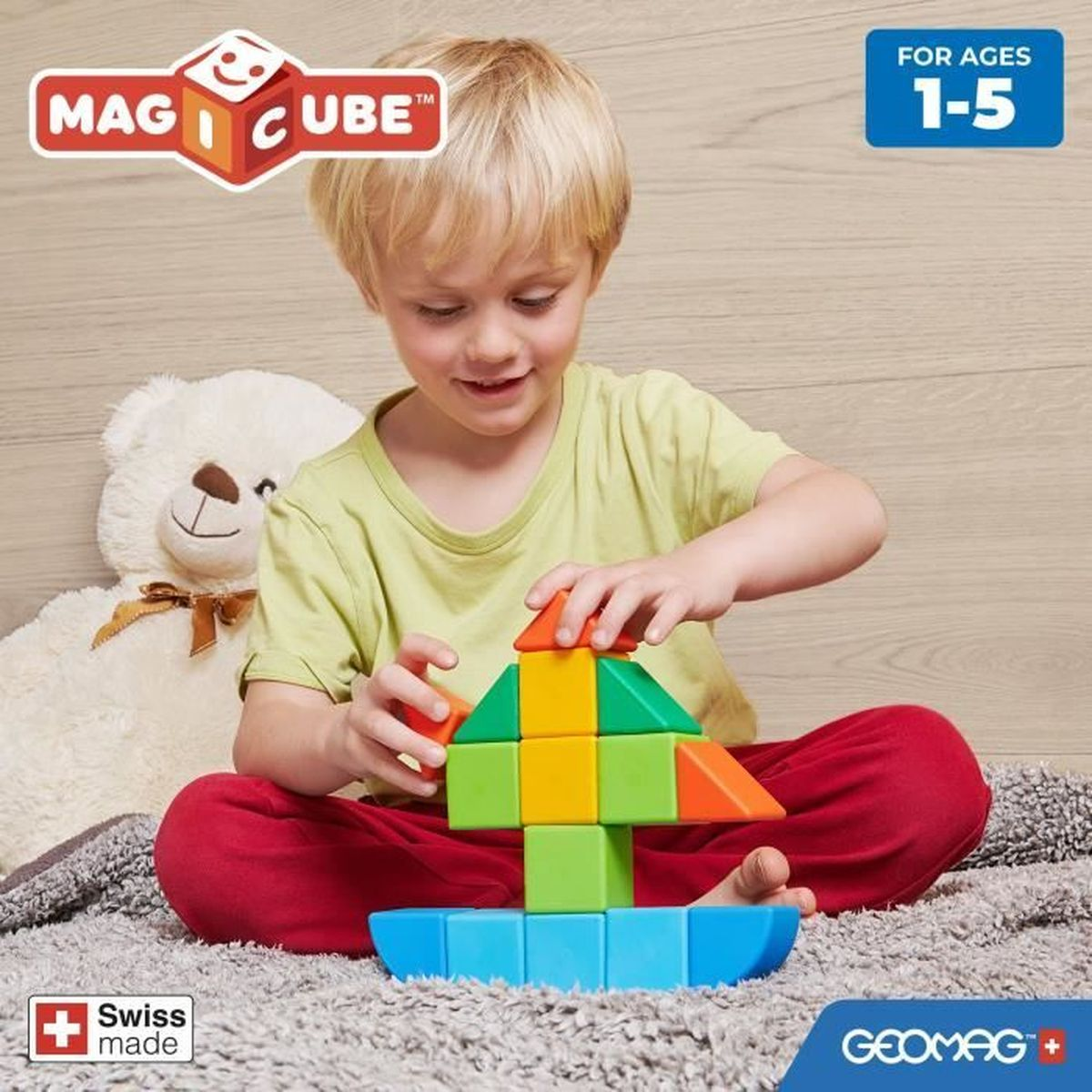 Un bambino gioca con blocchi colorati. Un orsacchiotto bianco è accanto a lui. I blocchi hanno forme diverse.