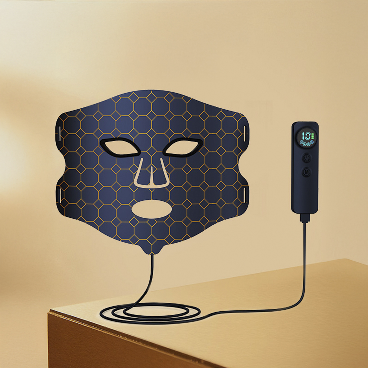 Eine dunkelblaue Gesichtsmaske mit goldenem geometrischen Muster. Ein Controller ist angeschlossen, der auf einer Holzoberfläche liegt, mit cremefarbenem Hintergrund.