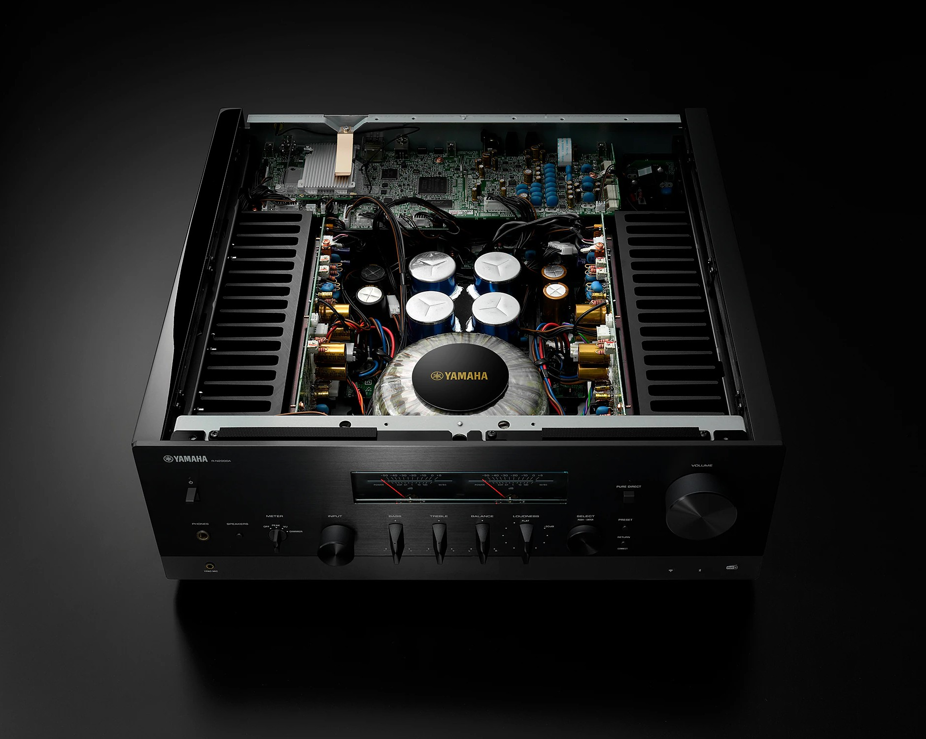 Açık bir Yamaha amplifikatörü, iç bileşenleri gösteriyor: devreler, kondansatörler ve merkezi bir transformatör. Siyah kasa.