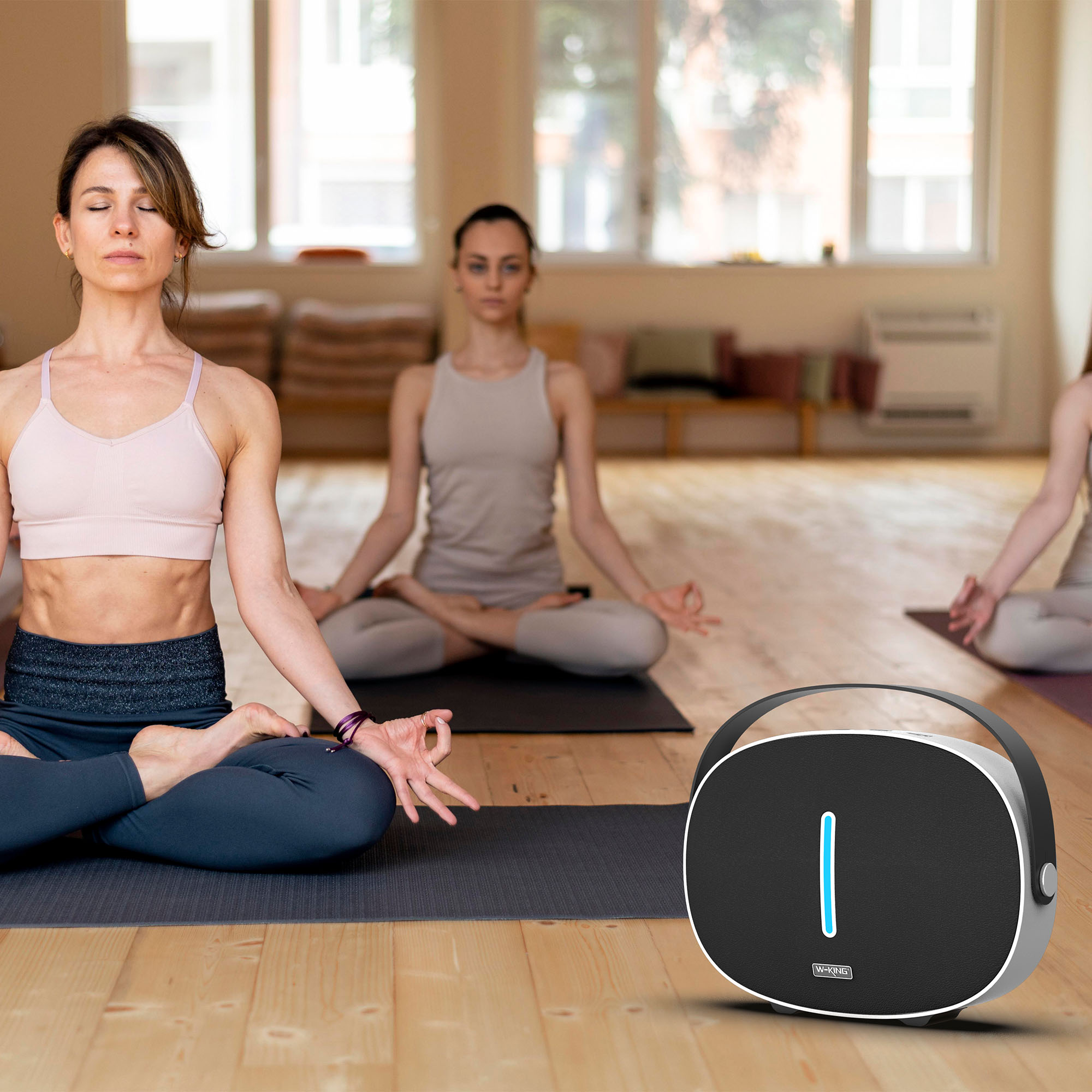 Yoga dersinde kadınlar, meditasyon yapıyor. Ön planda mavi ışıklı siyah bir hoparlör var.