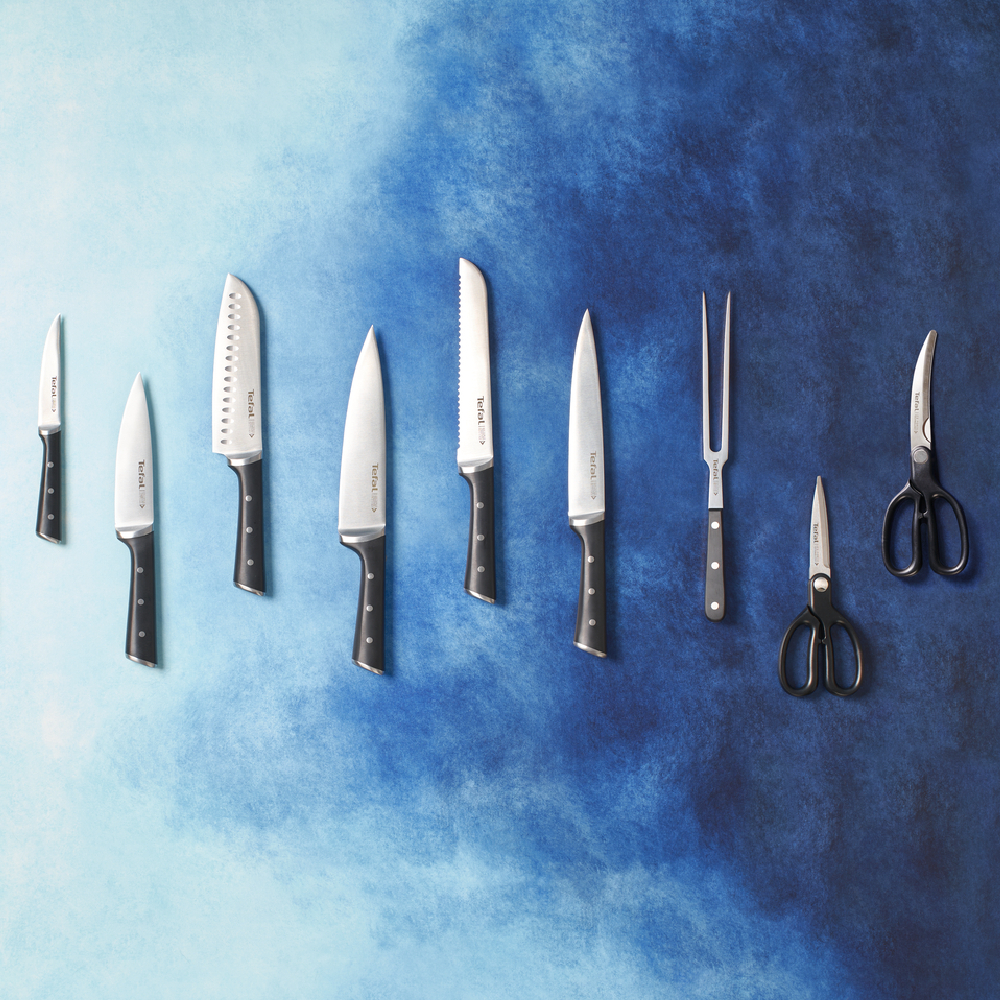 Kolekcja noży i nożyczek Tefal na niebieskim tle. Noże mają czarne uchwyty i srebrne ostrza.
