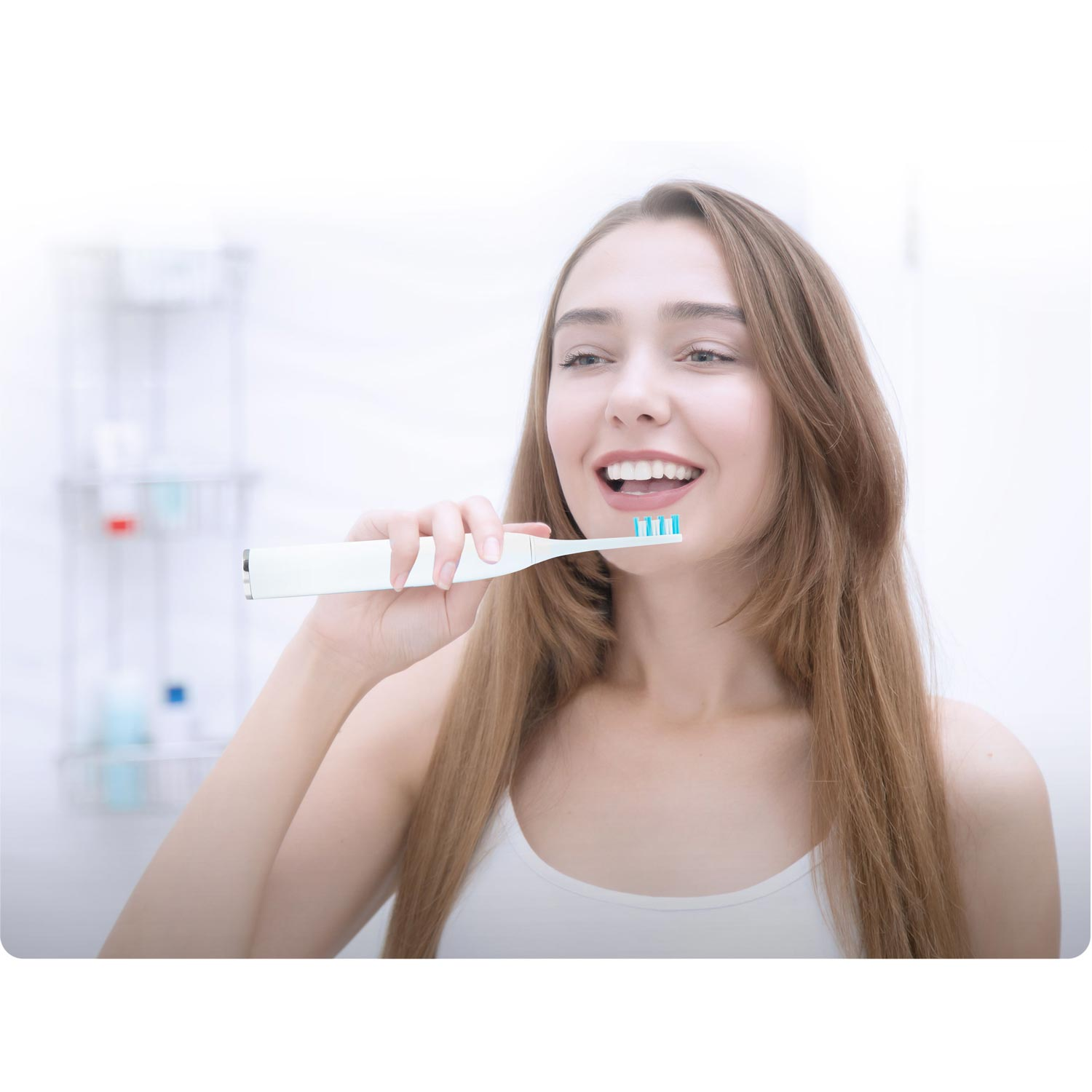 Kobieta myje zęby szczoteczką elektryczną. Uśmiecha się, pokazując zęby. Widoczne tło łazienki.