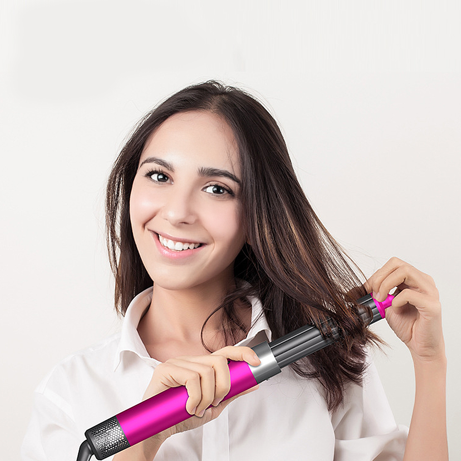Una donna sorride mentre usa uno strumento per lo styling dei capelli rosa e nero. Si tiene i capelli con lo strumento. Camicia bianca.