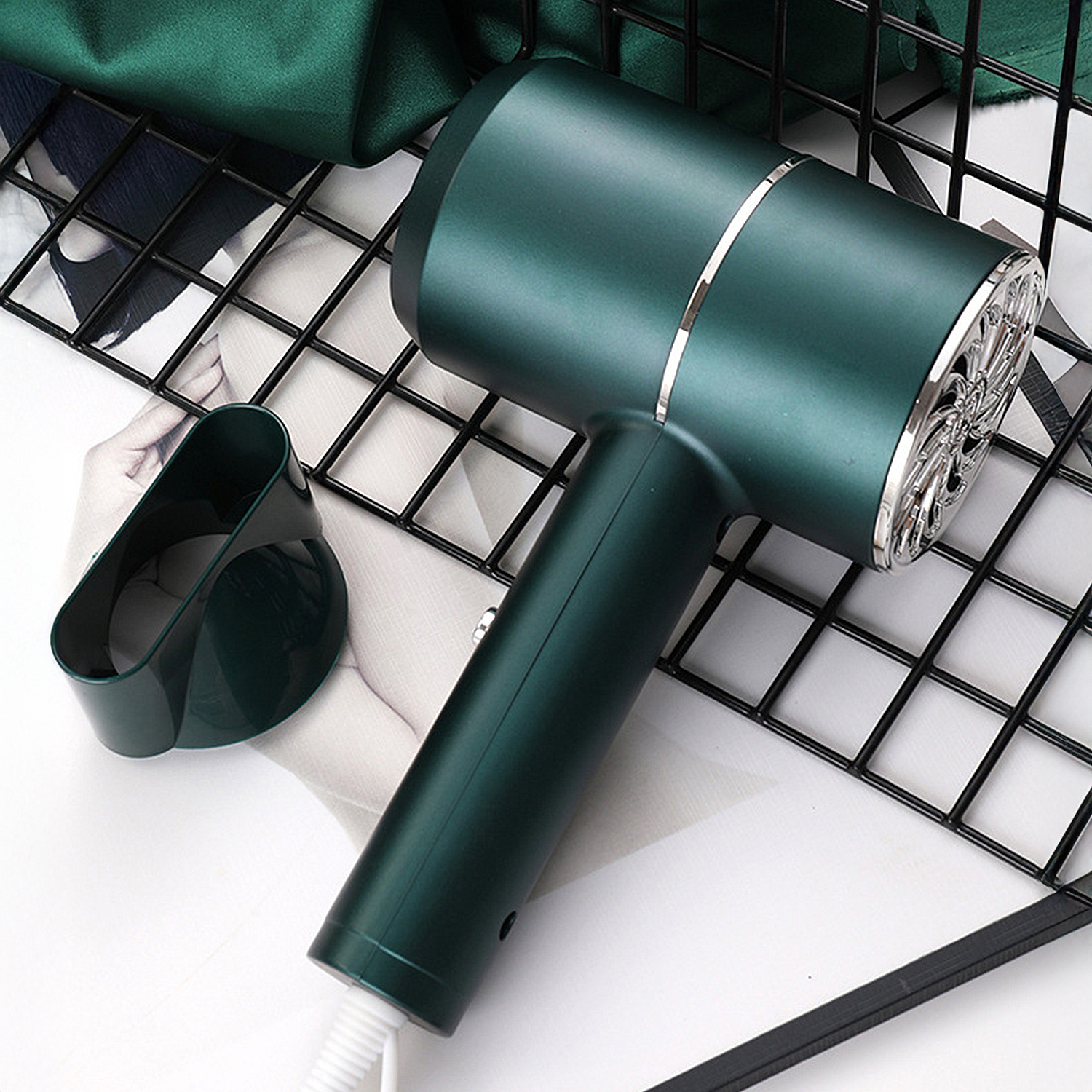 Un asciugacapelli verde acqua con ugello e manico, posizionato su una superficie bianca con una griglia nera e un panno verde.