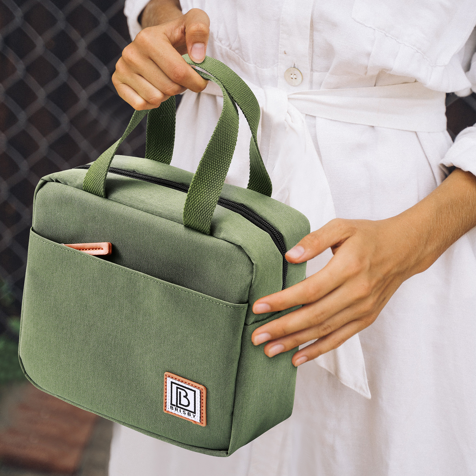 Een persoon houdt een groene tas vast met een bruine patch. De persoon draagt een witte jurk.