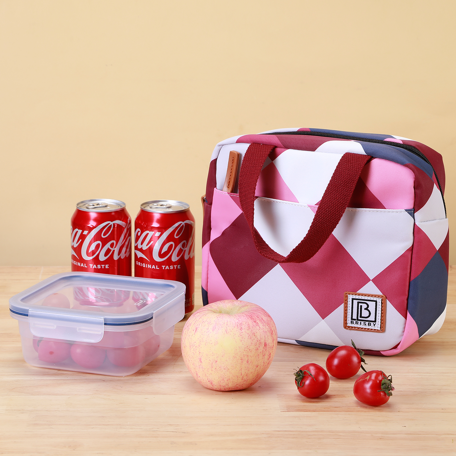 Een lunch met Coca-Cola blikjes, een lunchtas, een appel, kerstomaatjes en een bakje met eten op hout.