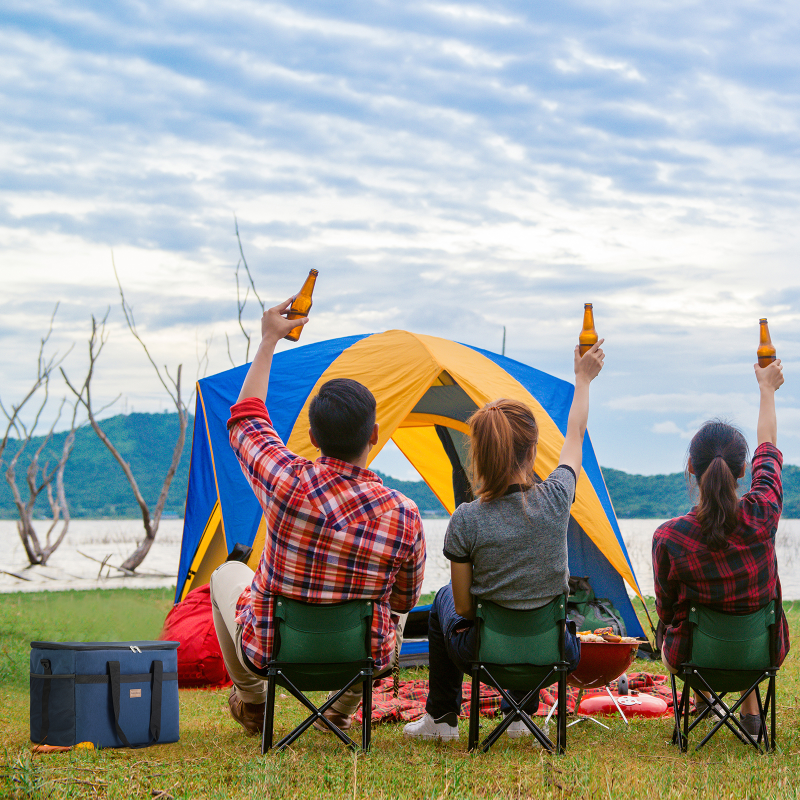 Drie mensen kamperen, houden bierflessen omhoog. Tent, meer en bergen op de achtergrond. Proost!