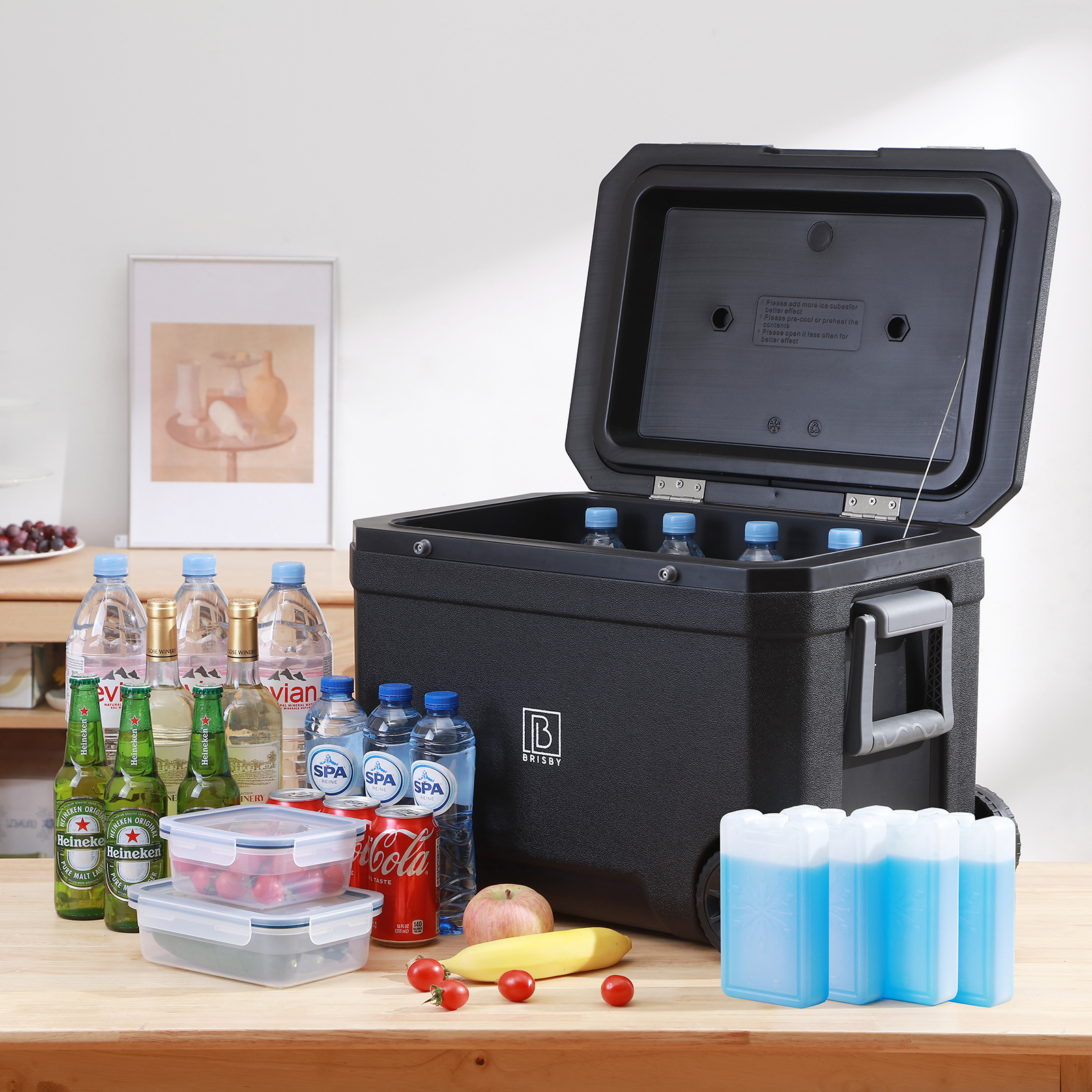 Een zwarte koeler met open deksel, flessen water en drankjes, fruit en voedselcontainers staan op een houten tafel.