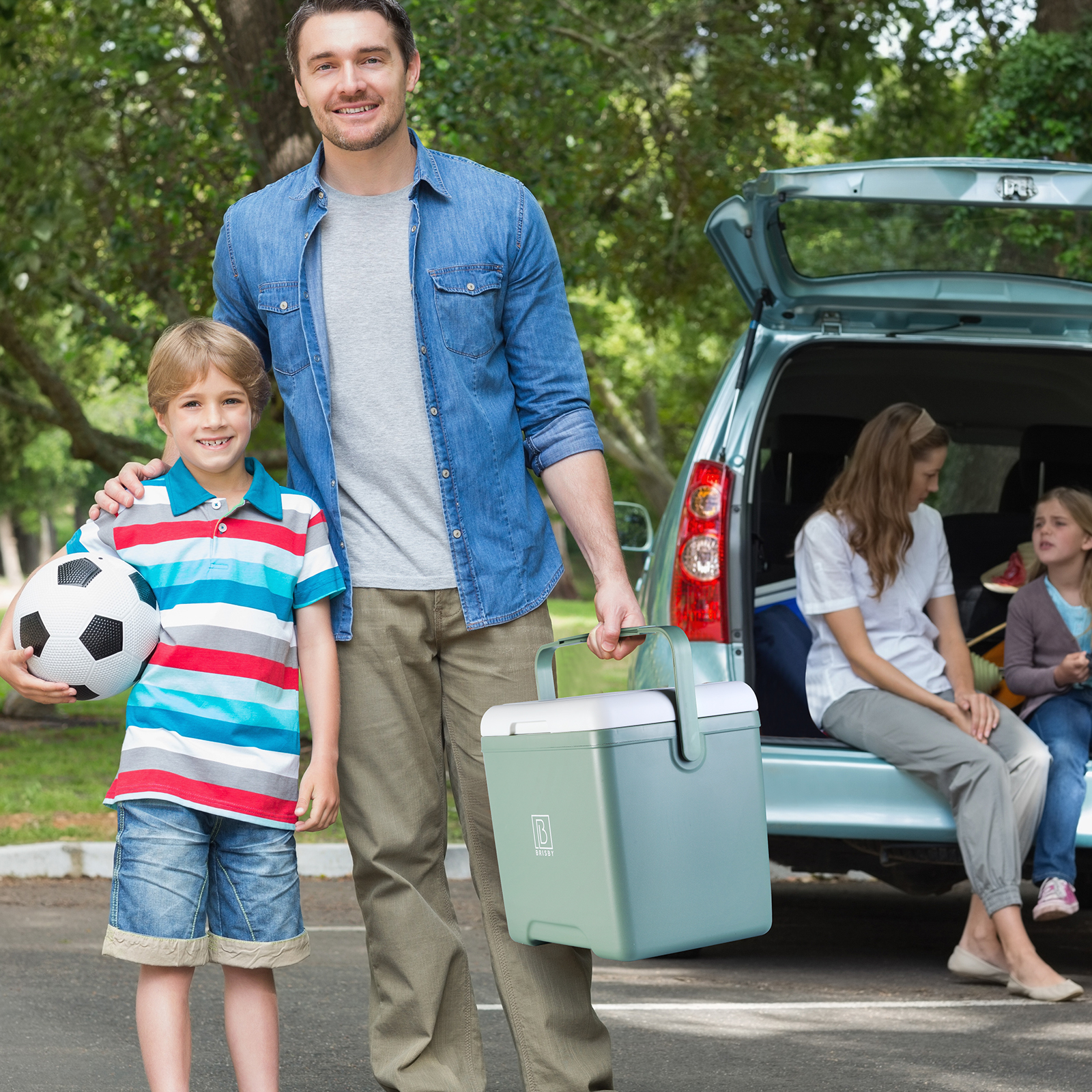Een man en een jongen met een voetbal en een koelbox, familiepicknick. Een vrouw en een meisje zitten in de auto.