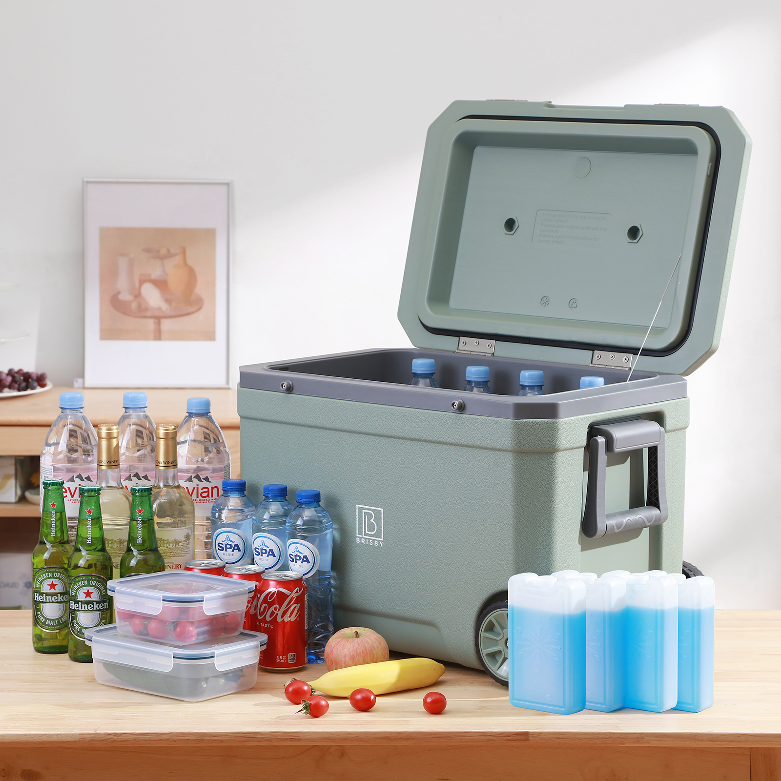 Een koeler met drankjes, eten en koelelementen op een tafel. Waterflessen, frisdrank, bier en fruit worden getoond.