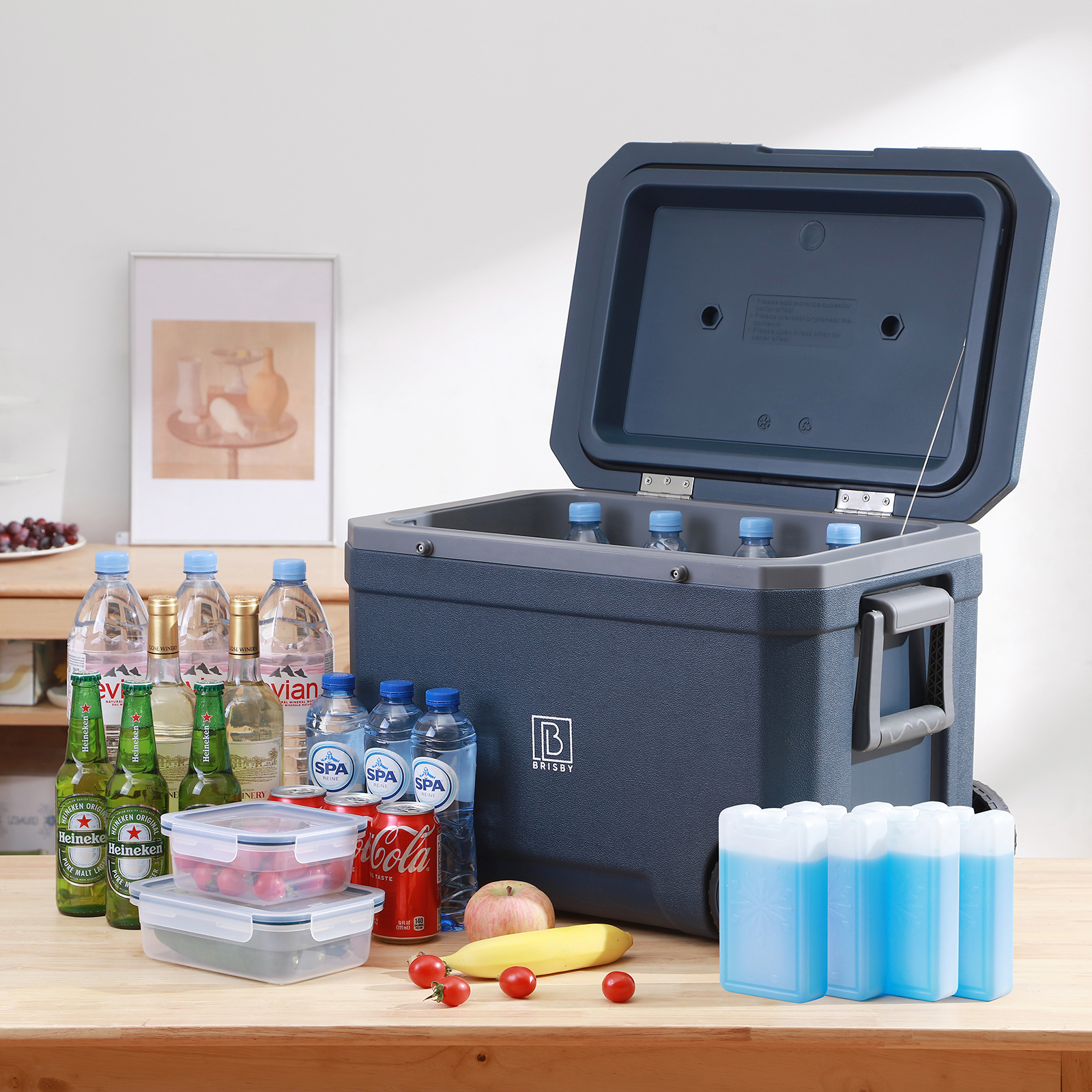 Een koelbox met drankjes, eten en koelelementen. Bevat waterflessen, bier, frisdrank, fruit en bakjes op een houten tafel.