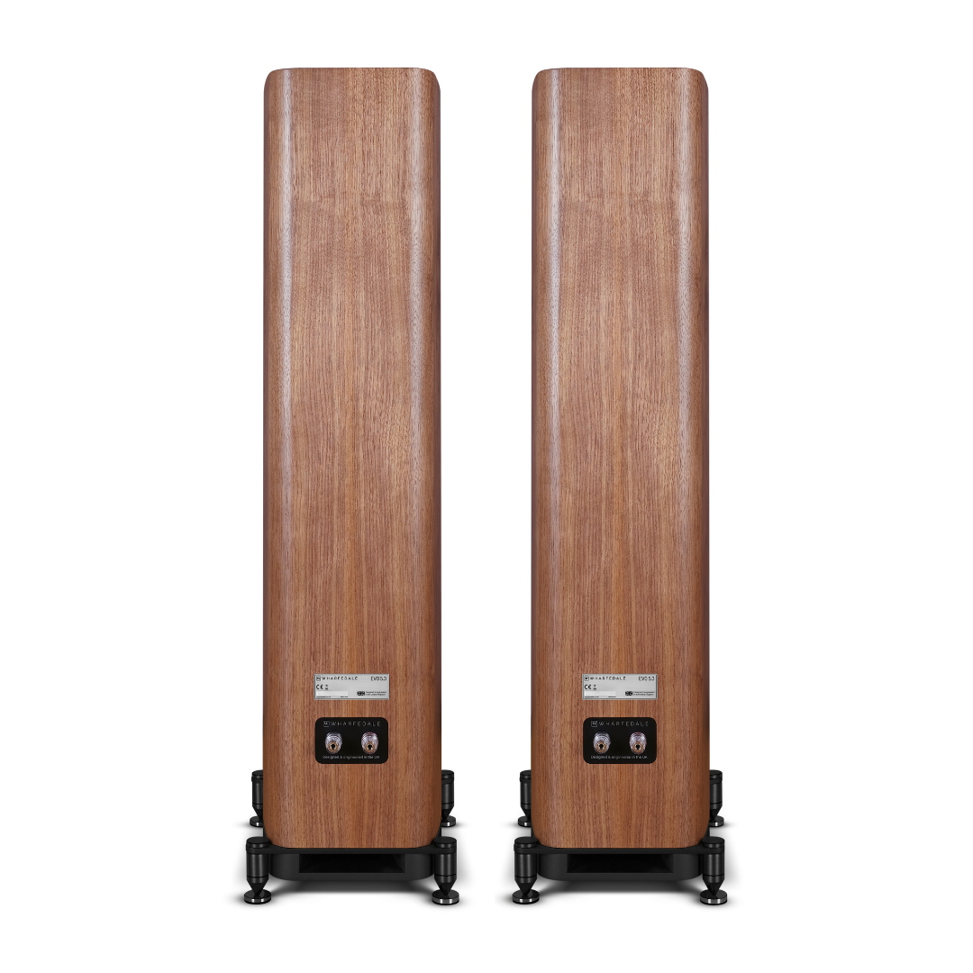 Two tall, wooden speakers stand on black bases against a white backdrop. Each has a label. The wood grain is visible.