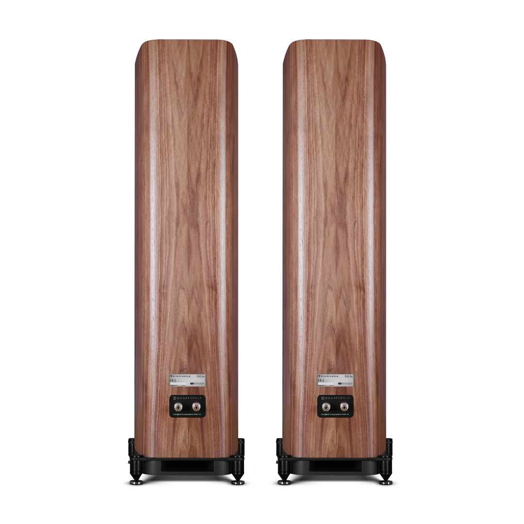 Twee hoge houten luidsprekers met een walnoot afwerking. Zwarte bases en labels zijn zichtbaar aan de achterkant. De achtergrond is wit.