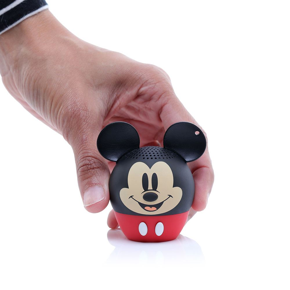 Una mano tiene in mano un altoparlante di Topolino. È nero con la parte inferiore rossa, un viso sorridente e due bottoni bianchi.
