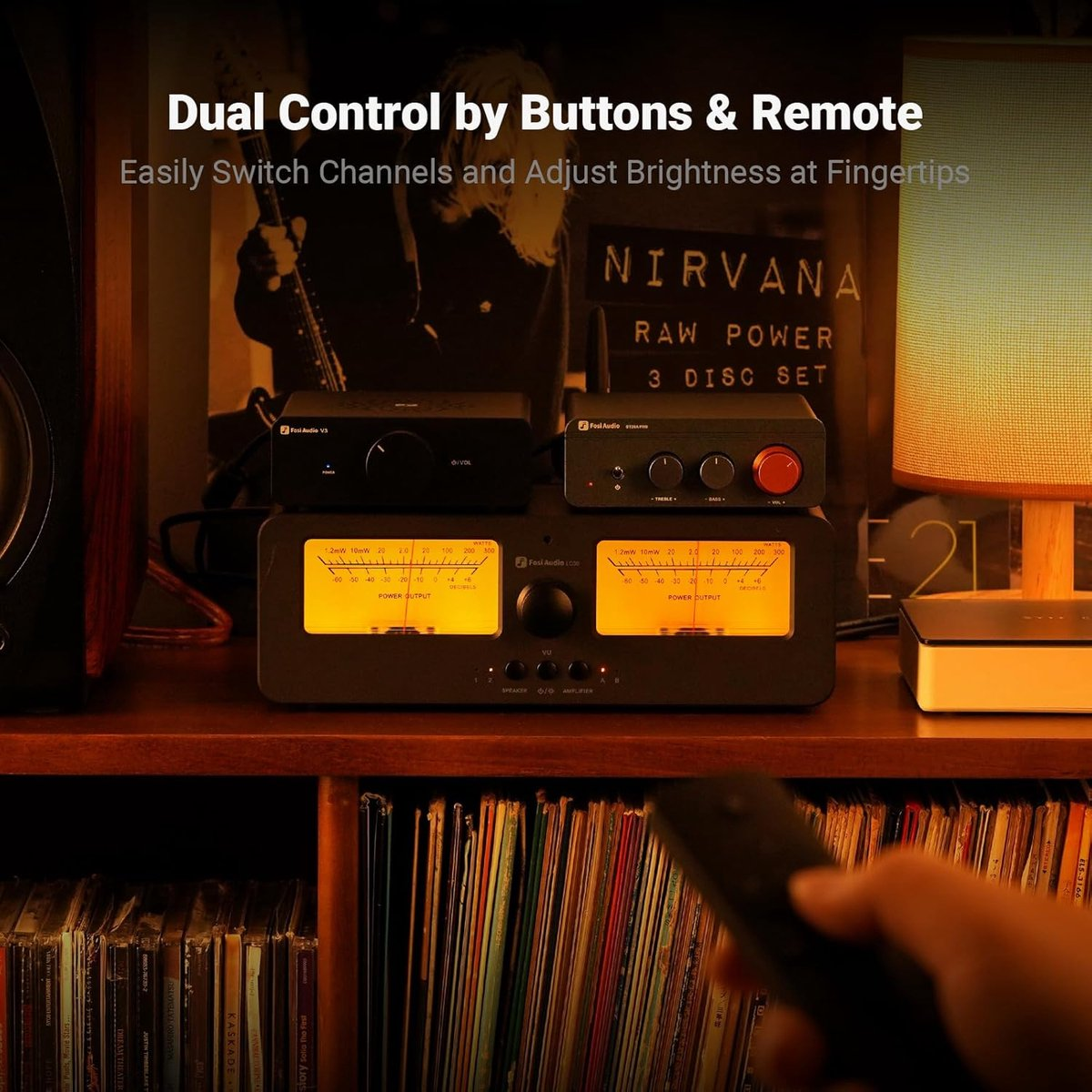 Une configuration audio avec amplificateurs, indicateurs VU et une affiche de l'album Nirvana. Une télécommande est tenue au premier plan.