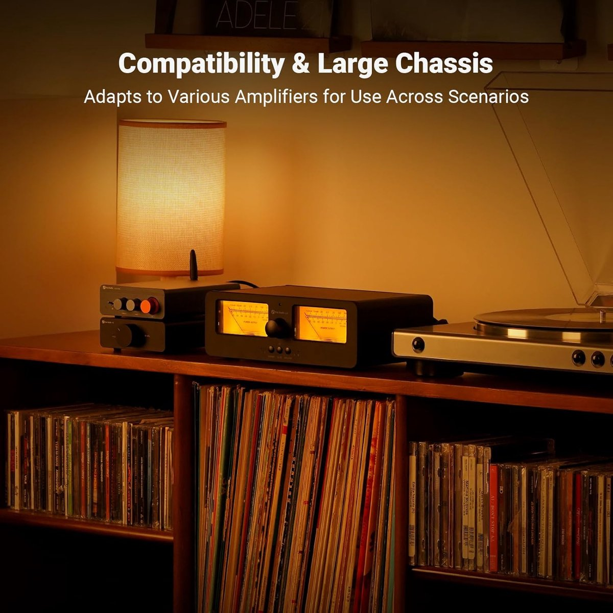 Une platine, des amplificateurs et des CD sont sur une étagère en bois. Une lampe est à gauche. La scène est de tons chauds.