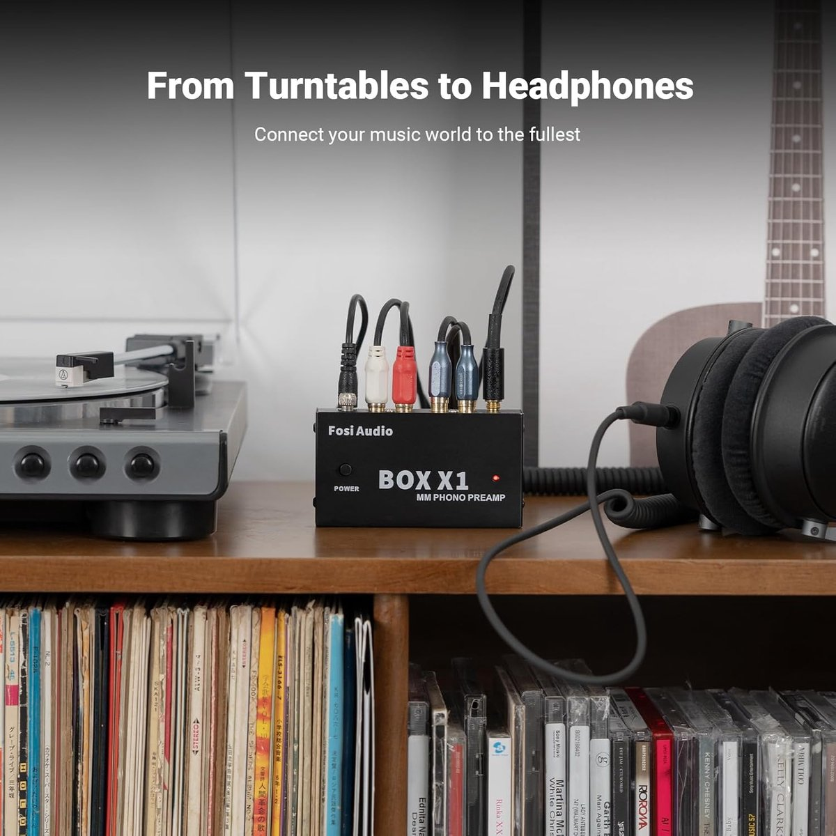 Gramofon, skrzynka audio, słuchawki i płyty CD na półce. Kable łączą urządzenia. Gitara widoczna w tle.