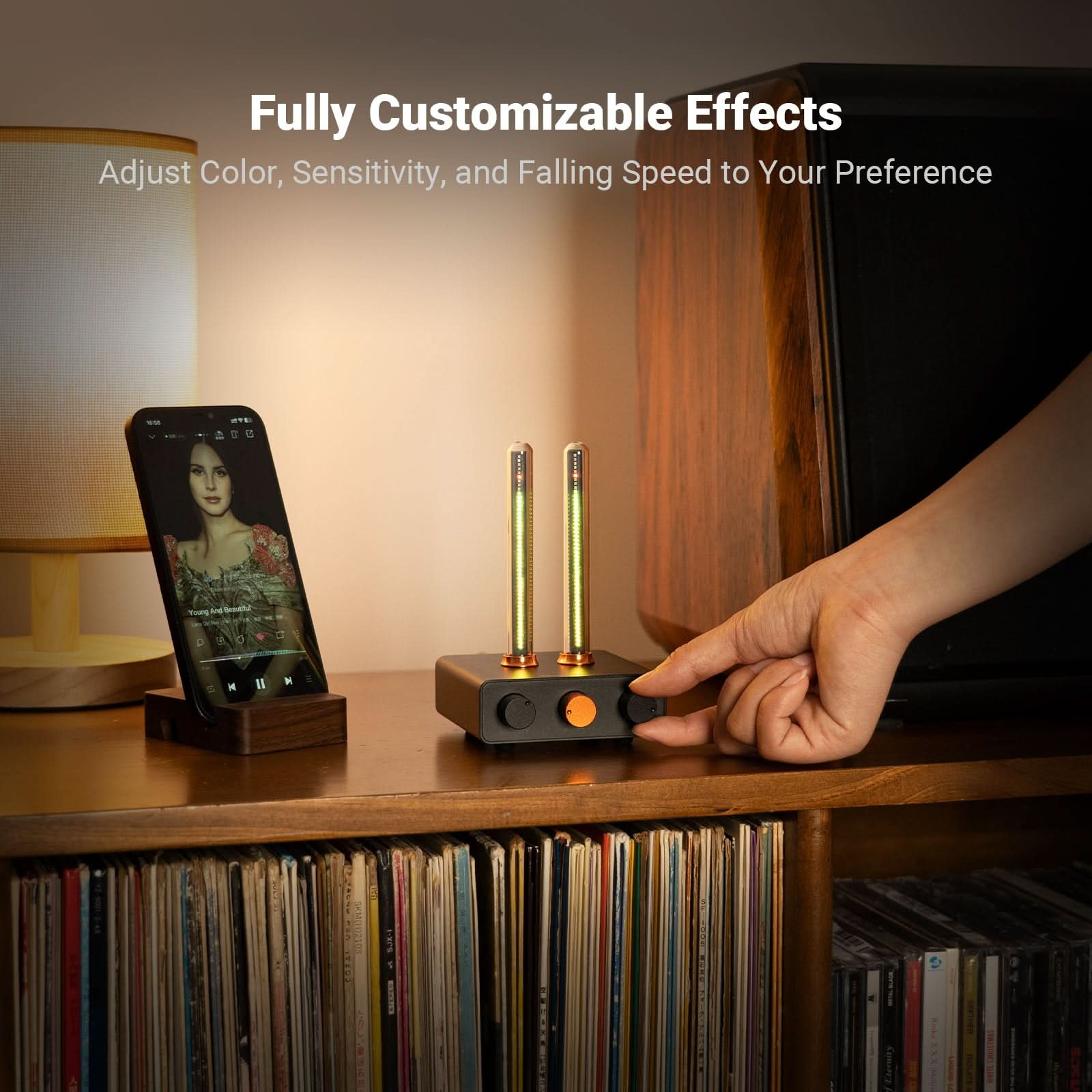 Une main ajuste un appareil avec deux tubes lumineux, un téléphone jouant de la musique et une collection de disques.