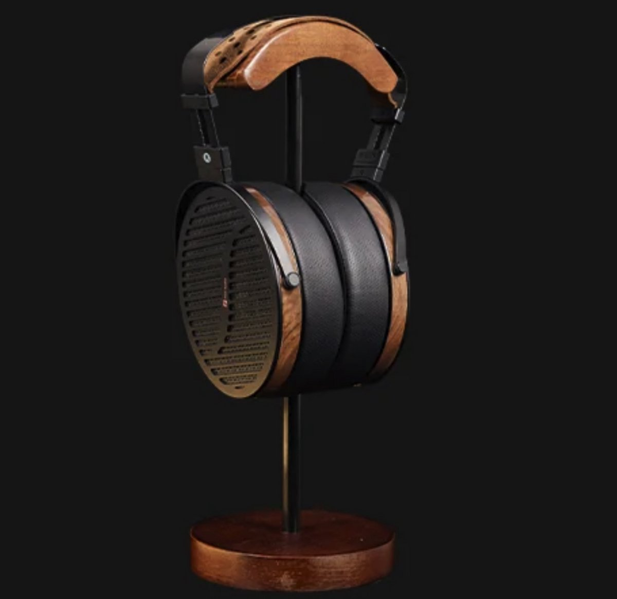 Headphones with wood and black accents on a stand. Dark background. Earpads are black leather. Stand is metal with a wood base.