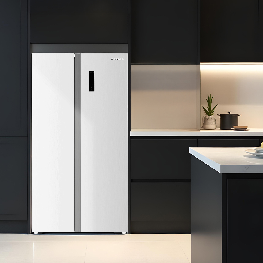 Nowoczesna biała lodówka stoi w ciemnej kuchni. Blat z rośliną i garnkiem jest widoczny w tle.