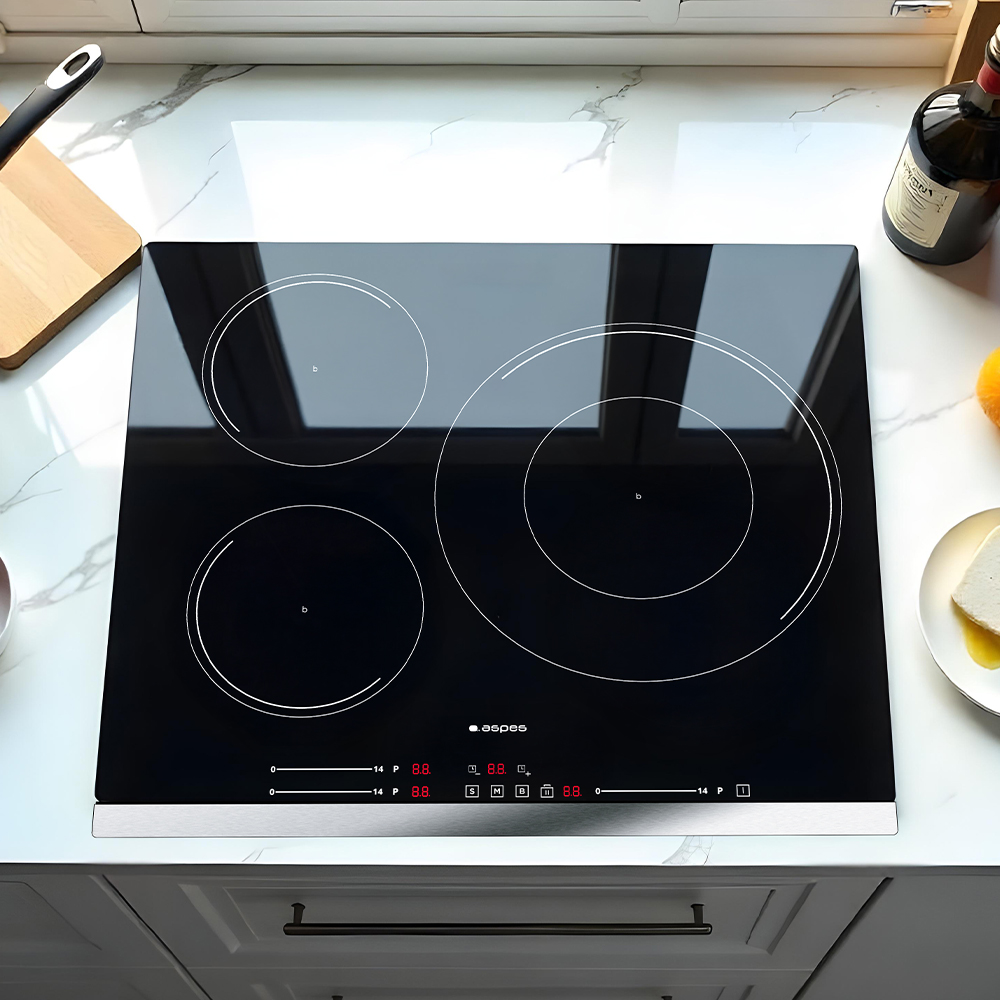 Czarna płyta indukcyjna z trzema okrągłymi strefami grzewczymi. Drewniana deska do krojenia i butelka wina w tle.