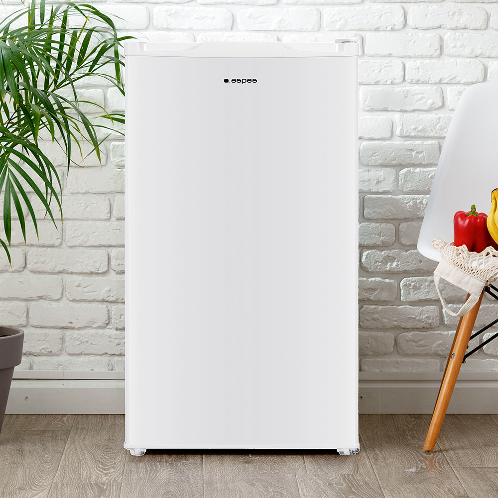 Refrigerador blanco con logotipo 'aspes'. Pimiento rojo y plátano en silla. Planta verde en maceta. Fondo de pared de ladrillo blanco.