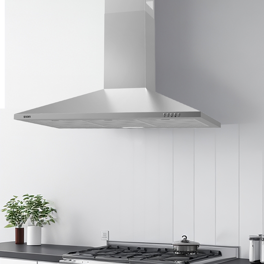Una campana extractora de acero inoxidable está montada sobre una estufa de gas. Debajo, se ven una planta y una olla. Las paredes blancas completan la escena.
