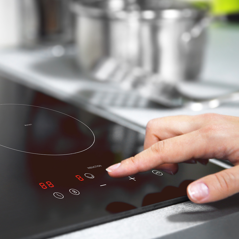 Una mano toca una cocina de inducción negra. Números rojos muestran 8 y 8. Una olla está en el fondo. Los controles de la estufa son visibles.