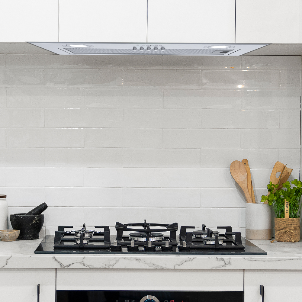 Una cocina moderna con una encimera negra, salpicadero blanco y campana extractora. Utensilios de madera y una planta en la encimera.