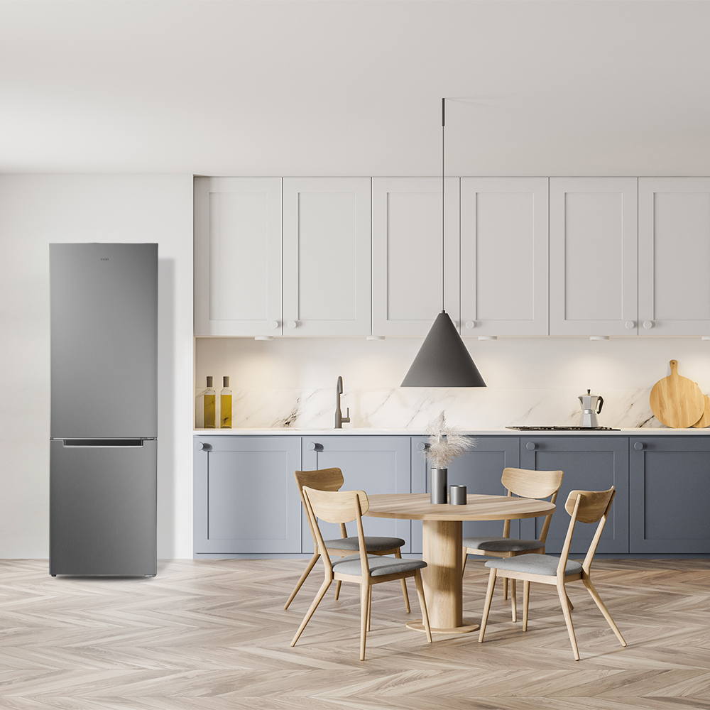 Una cocina moderna con un refrigerador gris, una mesa redonda con sillas y gabinetes. El suelo tiene un patrón de madera.